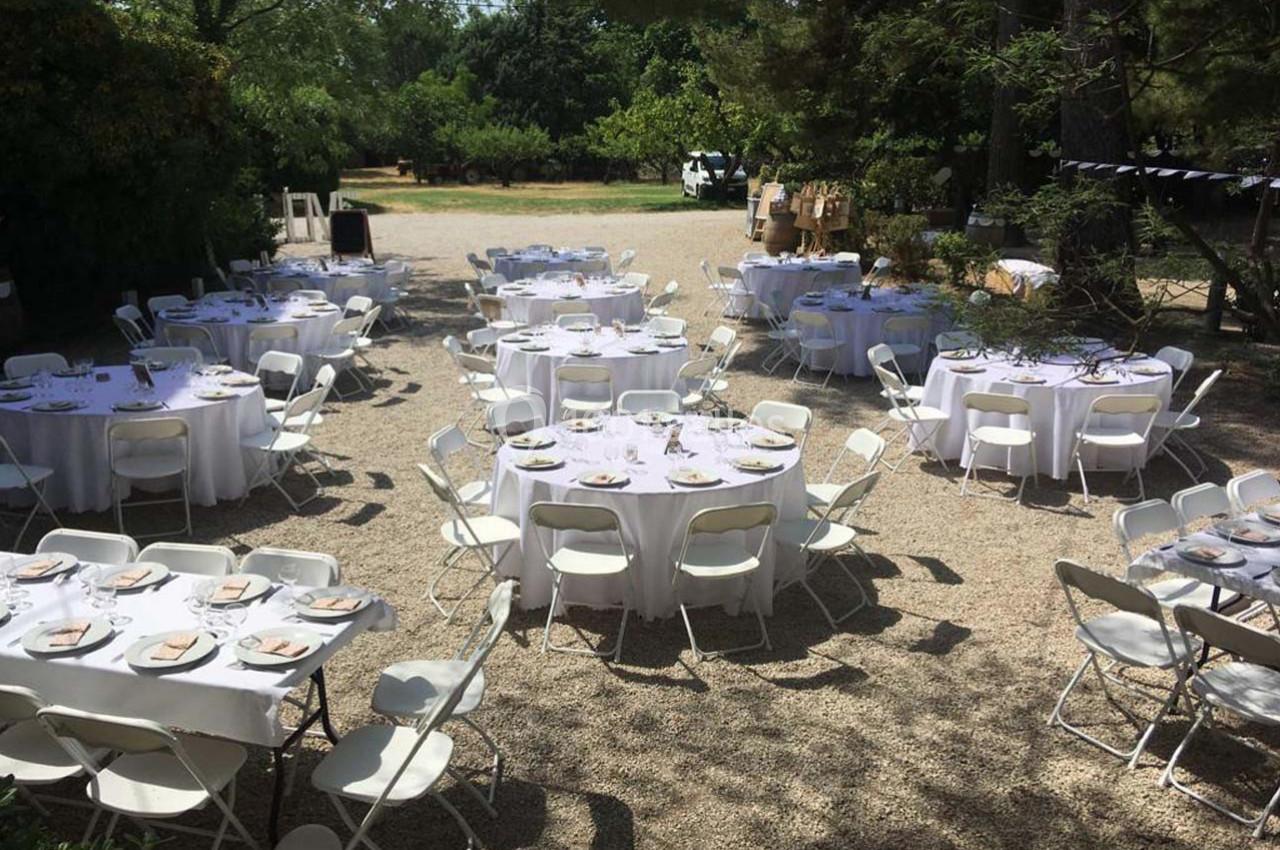 Tables rondes dressées avec nappes blanches et chaises pliantes dans un espace extérieur ombragé.