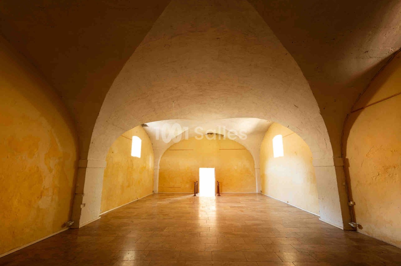 Salle voûtée aux murs jaunes avec un sol en carrelage, éclairée par des fenêtres et une porte ouverte au fond.