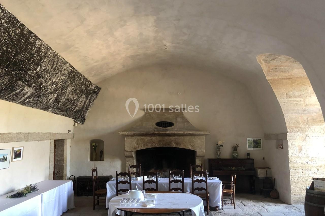 Salle voûtée ancienne avec cheminée en pierre, tables dressées avec nappes blanches et décorations simples.
