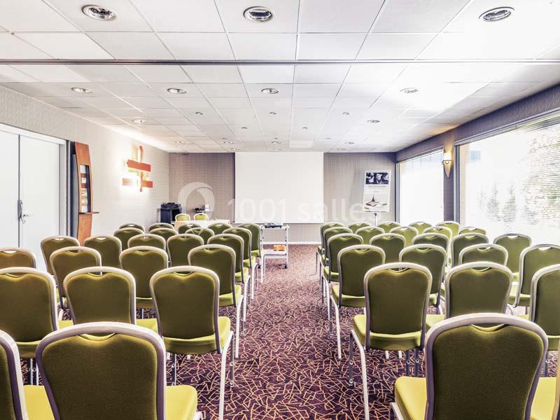 Salle de conférence lumineuse avec des rangées de chaises vertes face à un écran de projection blanc.