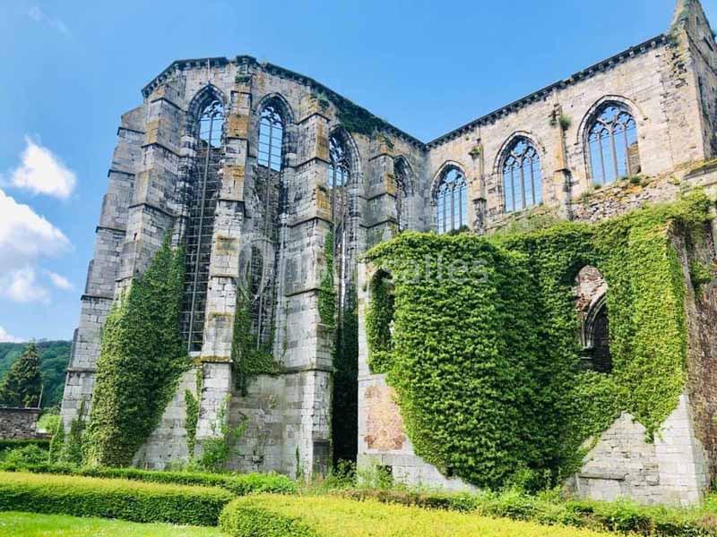Ruines d'une abbaye médiévale avec des murs recouverts de lierre, entourée de verdure sous un ciel bleu.