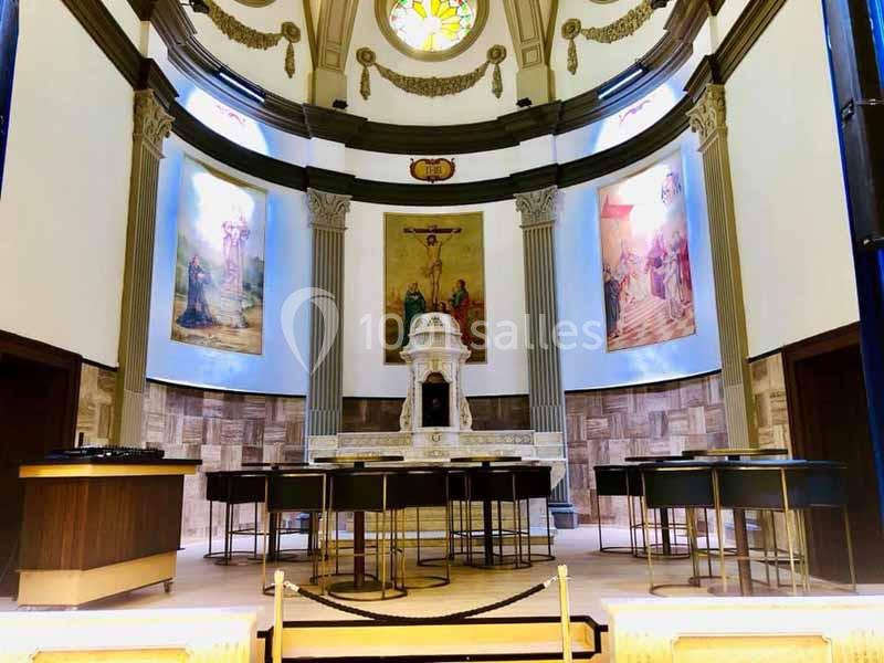 Intérieur d'une chapelle avec un autel central, colonnes, fresques religieuses et mobilier moderne.