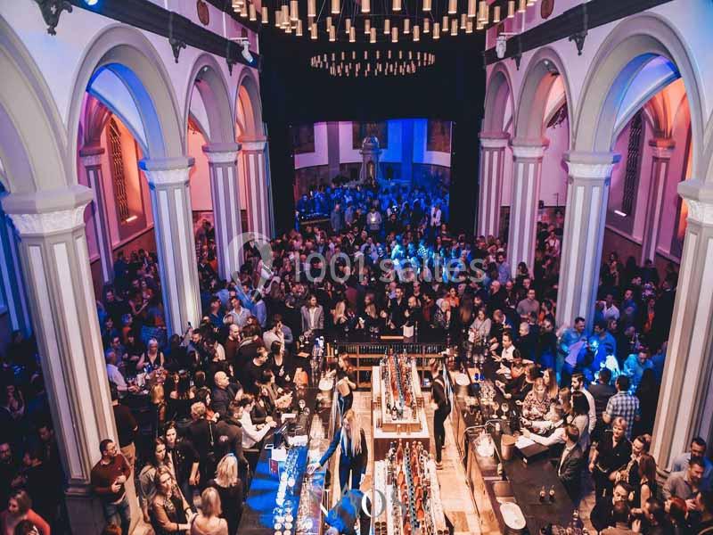 Salle bondée avec des arches illuminées, un bar central et des personnes socialisant dans une ambiance festive.