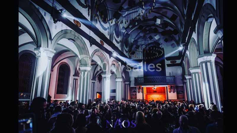 Foule rassemblée dans une église aux voûtes éclairées par des lumières colorées, ambiance nocturne.