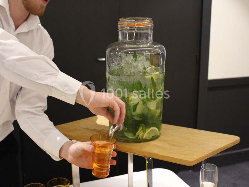 Un serveur remplit un verre avec une boisson à base de citron, menthe et glace, depuis un grand distributeur en verre.