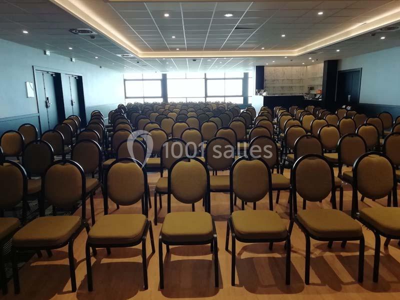 Salle de conférence avec des rangées de chaises vides alignées sous un plafond éclairé par des spots.
