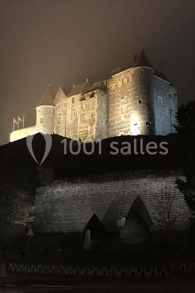 Château en pierre illuminé la nuit, entouré de remparts et partiellement enveloppé de brume.
