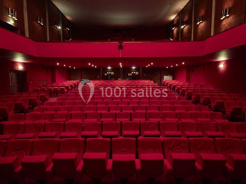 Salle de cinéma vide avec des rangées de fauteuils rouges et un éclairage tamisé.