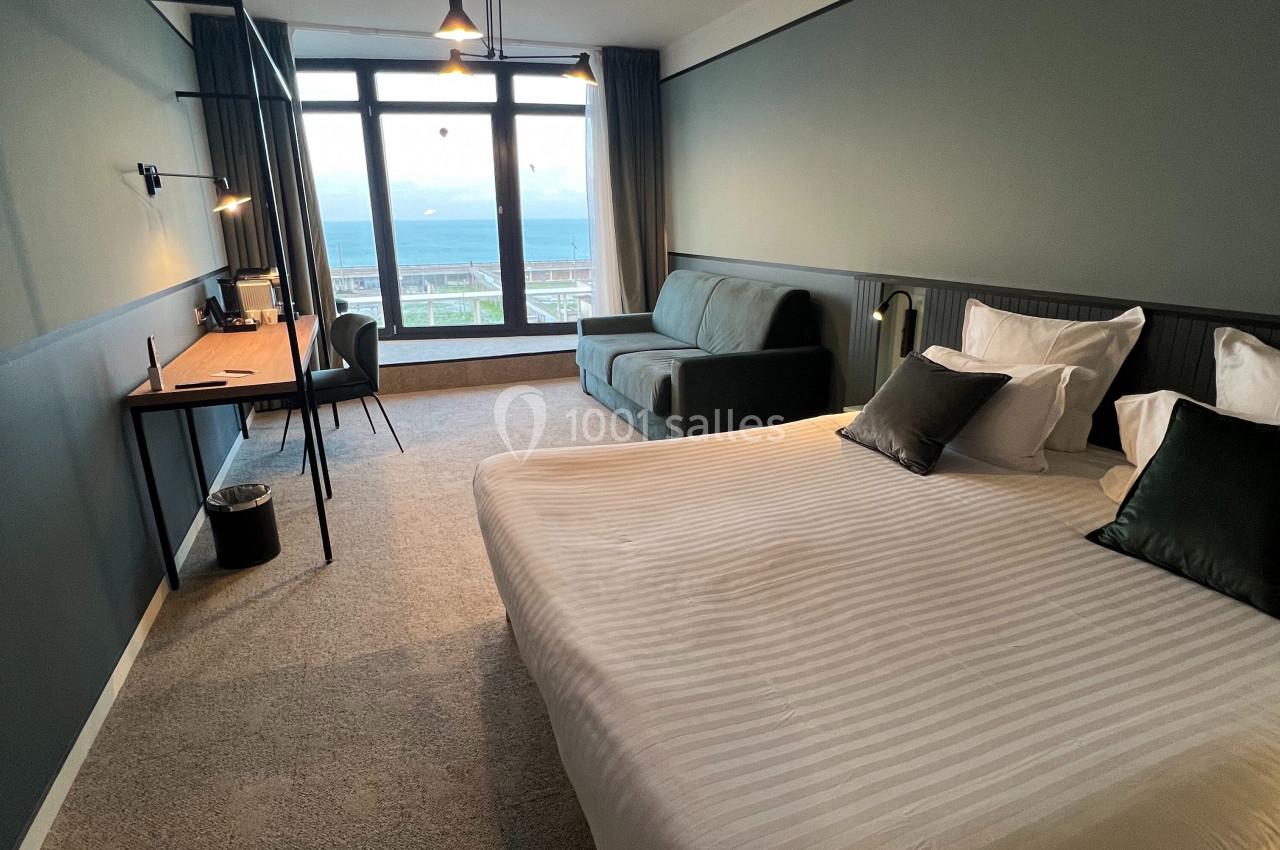 Chambre d'hôtel moderne avec lit double, bureau, canapé et grande fenêtre offrant une vue dégagée.