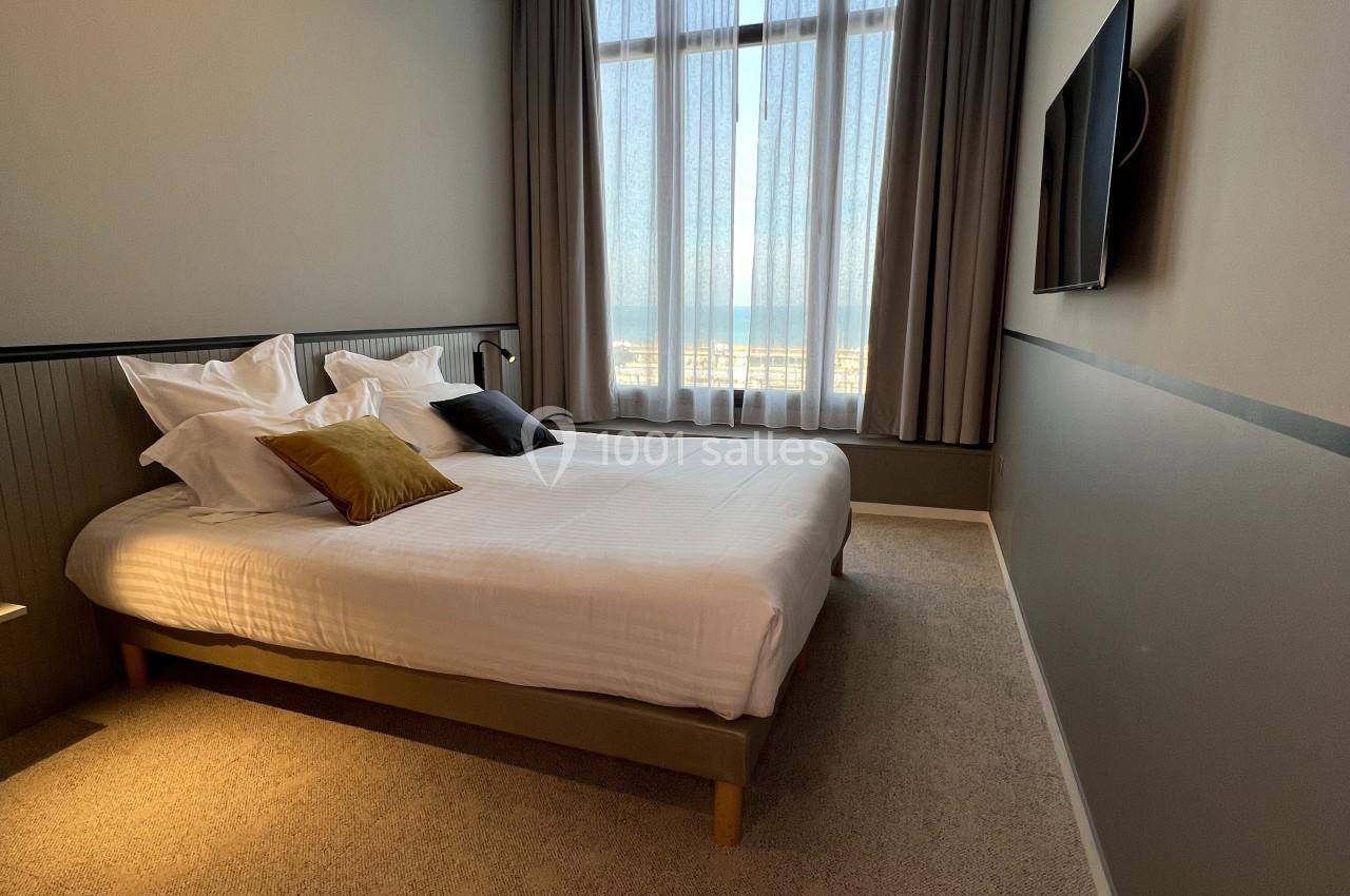 Chambre moderne avec lit double, grande fenêtre avec rideaux, éclairage suspendu et télévision murale.