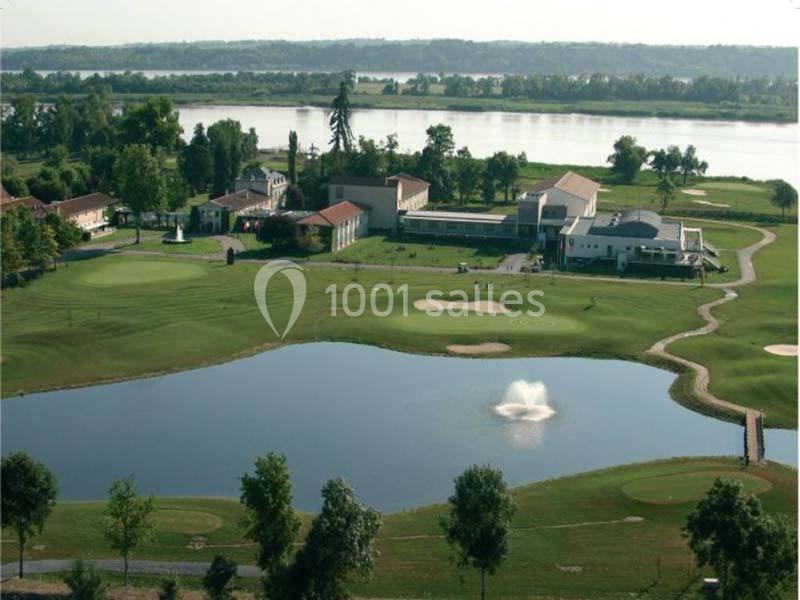Vue aérienne d'un terrain de golf avec un étang central, une fontaine et des bâtiments en arrière-plan près d'une rivière.