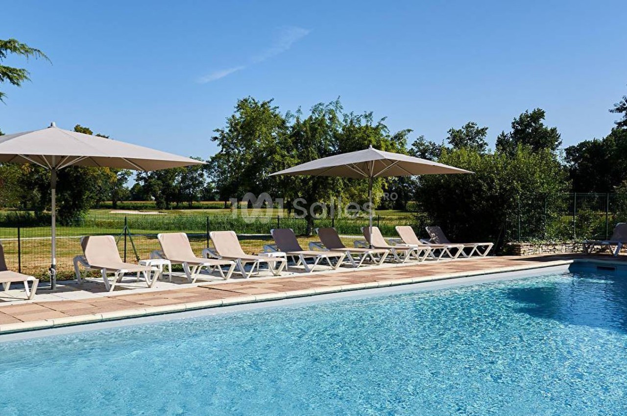 Piscine extérieure avec transats et parasols, entourée de verdure sous un ciel dégagé.