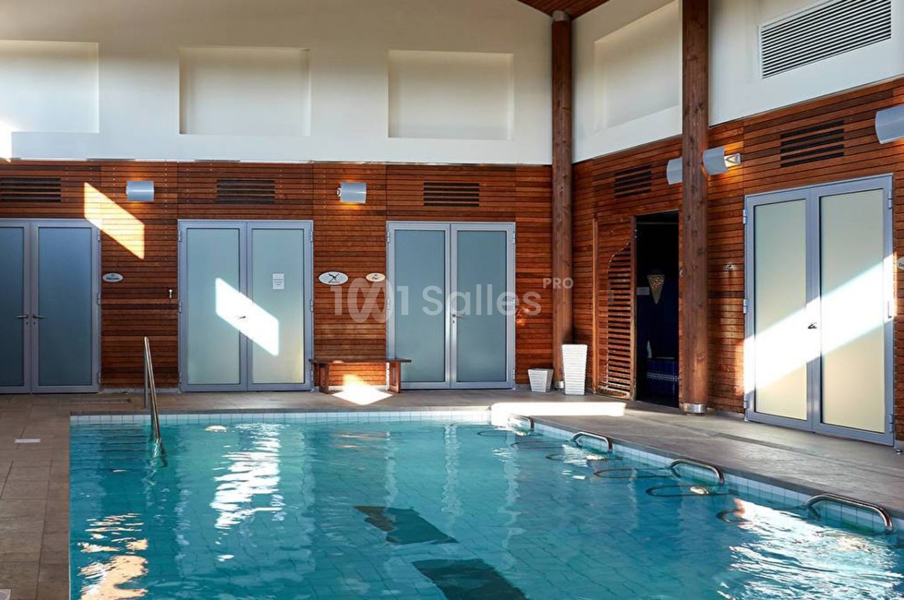 Piscine intérieure avec murs en bois, éclairée par la lumière naturelle, entourée de cabines et d'équipements.