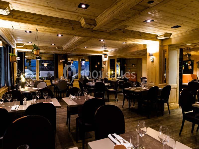 Salle de restaurant chaleureuse avec tables dressées, éclairage tamisé et décoration en bois.