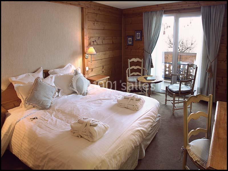 Chambre avec lit double, murs en bois, chaises près d'une table et balcon donnant sur l'extérieur.