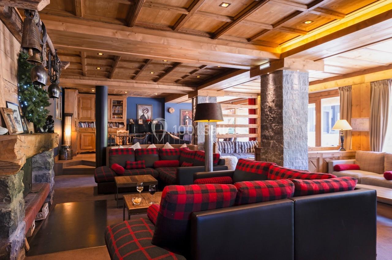 Salon chaleureux avec canapés à motifs écossais, cheminée en pierre, éclairage doux et décor en bois.