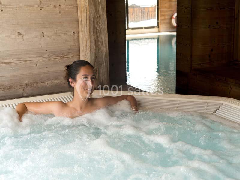 Femme relaxant dans un jacuzzi en bois, avec une piscine visible en arrière-plan.