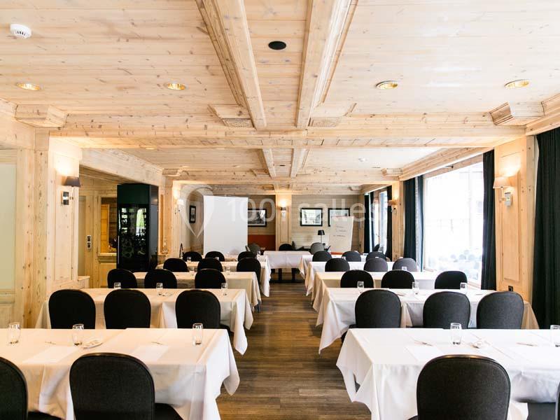 Salle de réunion lumineuse avec tables dressées, chaises noires et plafond en bois sculpté.