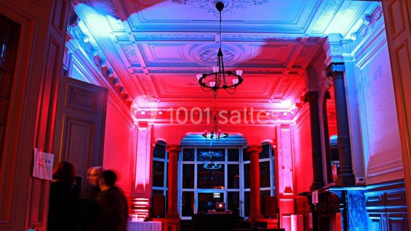 Location salle Farciennes (Hainaut) - Château Oxyjeunes #2 Salle avec un plafond orné, éclairée par des lumières rouges et bleues, avec des silhouettes floues au premier plan.