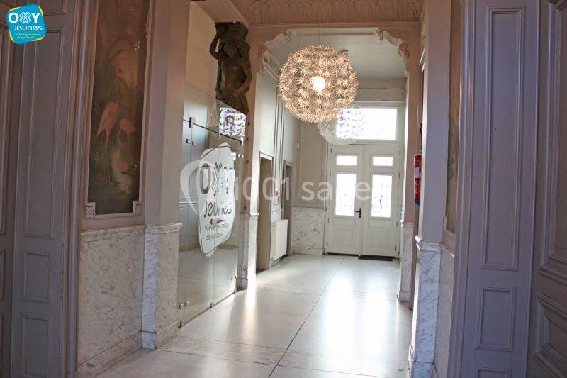 Location salle Farciennes (Hainaut) - Château Oxyjeunes #5 Entrée lumineuse avec portes vitrées, lustre moderne et murs ornés de moulures et de panneaux décoratifs.