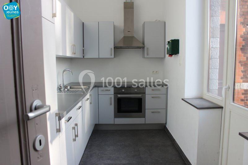 Location salle Farciennes (Hainaut) - Château Oxyjeunes #11 Cuisine moderne avec meubles blancs, évier en inox, plaque de cuisson, hotte et fenêtre laissant entrer la lumière.