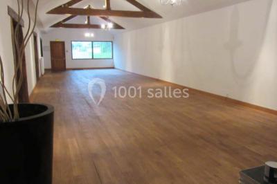 Salle lumineuse avec grandes fenêtres, mobilier en rotin gris et poutres apparentes, donnant sur un espace extérieur…