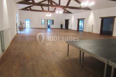 Salle lumineuse avec grandes fenêtres, mobilier en rotin gris et poutres apparentes, donnant sur un espace extérieur…