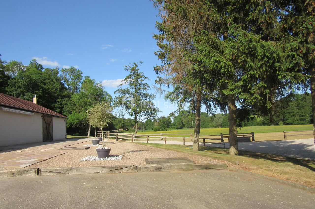 Cour extérieure avec graviers, arbres, clôtures en bois et bâtiment à gauche, sous un ciel dégagé.