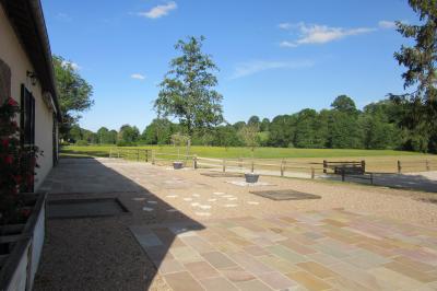 Salle lumineuse avec grandes fenêtres, mobilier en rotin gris et poutres apparentes, donnant sur un espace extérieur…