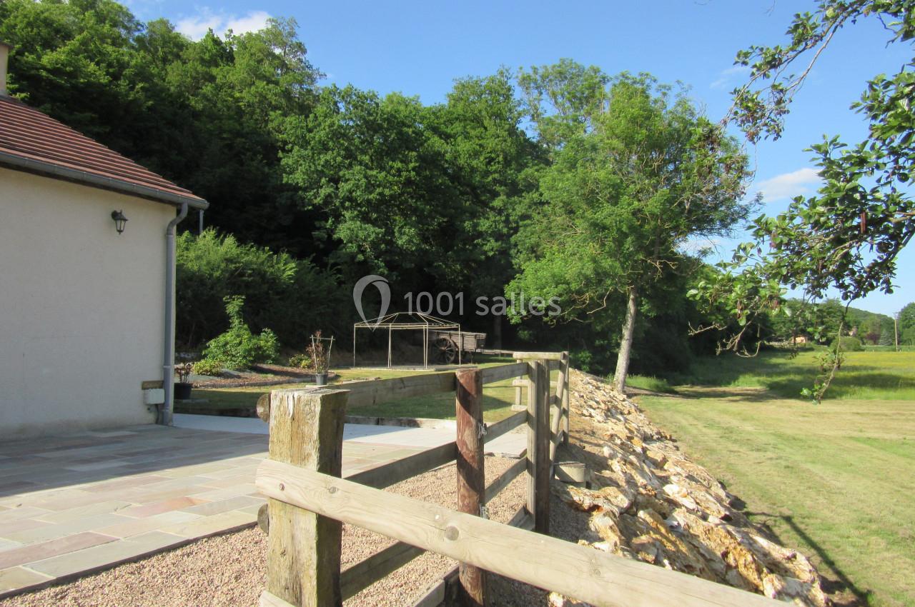 Clôture en bois bordant une terrasse pavée près d'une maison, avec un jardin verdoyant et des arbres en arrière-plan.