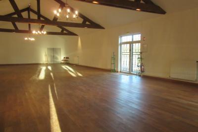 Salle lumineuse avec grandes fenêtres, mobilier en rotin gris et poutres apparentes, donnant sur un espace extérieur…