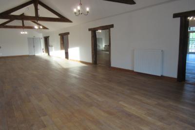 Salle lumineuse avec grandes fenêtres, mobilier en rotin gris et poutres apparentes, donnant sur un espace extérieur…