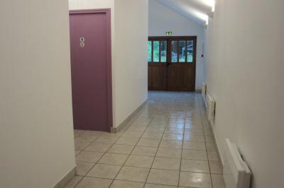 Salle lumineuse avec grandes fenêtres, mobilier en rotin gris et poutres apparentes, donnant sur un espace extérieur…