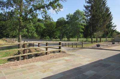 Salle lumineuse avec grandes fenêtres, mobilier en rotin gris et poutres apparentes, donnant sur un espace extérieur…