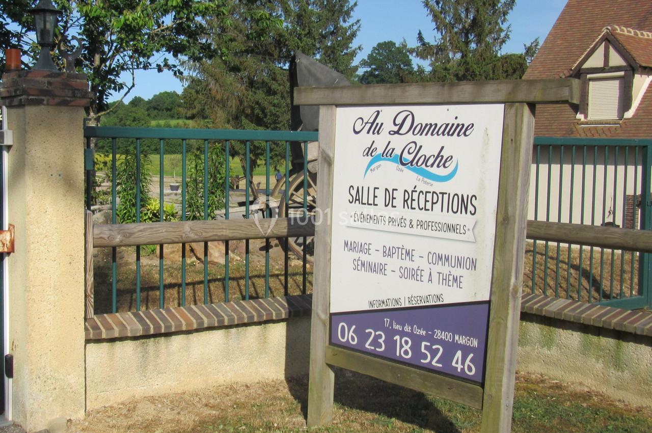 Panneau en bois indiquant ’Au Domaine de la Cloche’, salle de réceptions, devant une clôture et un paysage rural.