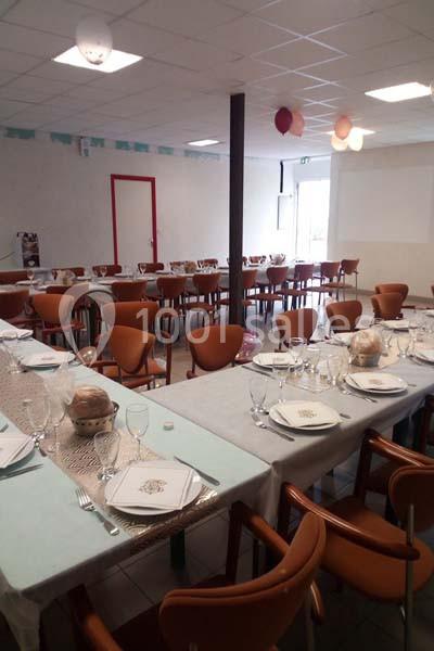 Salle décorée avec des tables dressées pour un repas, comprenant assiettes, verres, couverts et pain.