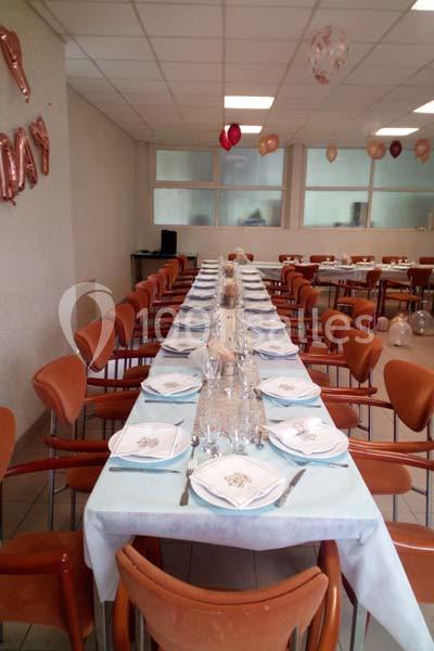 Salle décorée avec une longue table dressée pour un repas, entourée de chaises et ornée de ballons suspendus.