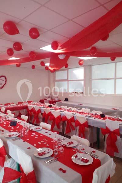 Salle décorée en rouge et blanc avec des tables dressées pour un événement, ornées de nappes, rubans et ballons.
