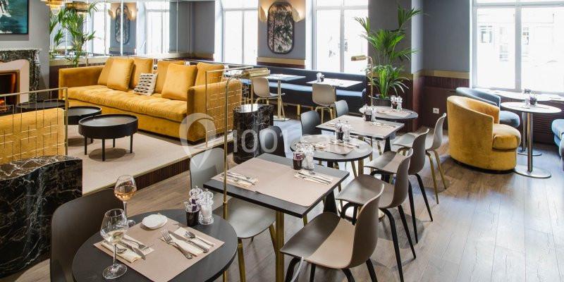 Salle de restaurant moderne avec tables dressées, chaises design, canapés jaunes et grandes fenêtres lumineuses.