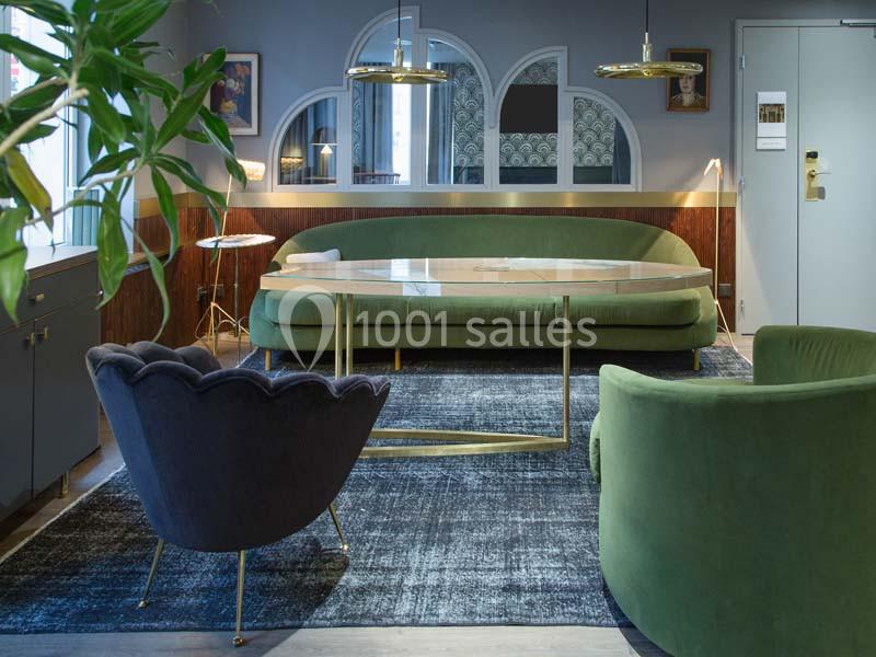 Salon moderne avec canapé vert, fauteuils assortis, table basse en verre et éléments décoratifs élégants.