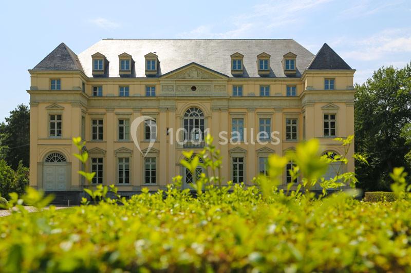 Façade d'un bâtiment historique jaune à plusieurs étages, entouré de verdure sous un ciel bleu.