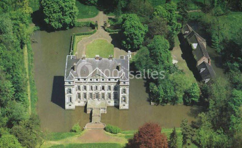Vue aérienne d'un château entouré d'eau et de verdure, avec des bâtiments annexes à proximité.