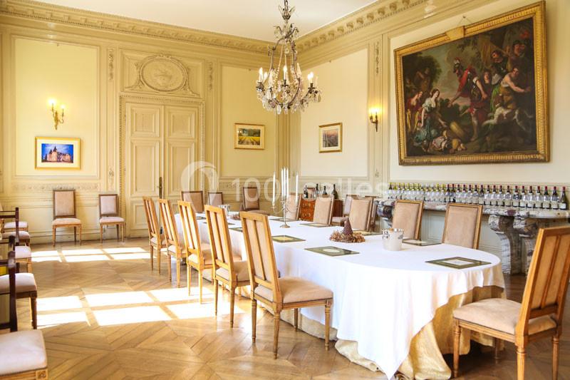 Salle élégante avec grande table ovale dressée, chaises en bois, lustre, parquet et tableaux décorant les murs.