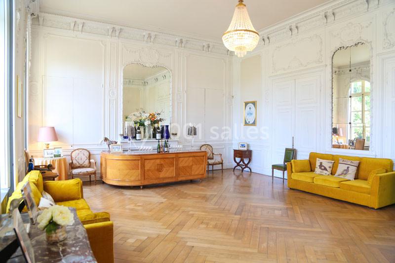 Salon lumineux avec parquet en bois, canapés jaunes, lustre, miroir et mobilier classique dans un décor élégant.