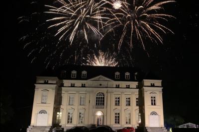 Un couple regarde un feu d'artifice illuminant le ciel nocturne avec des éclats de lumière colorés.