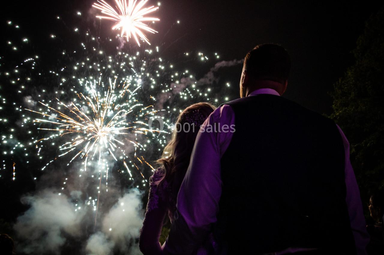 Un couple regarde un feu d'artifice illuminant le ciel nocturne avec des éclats de lumière colorés.