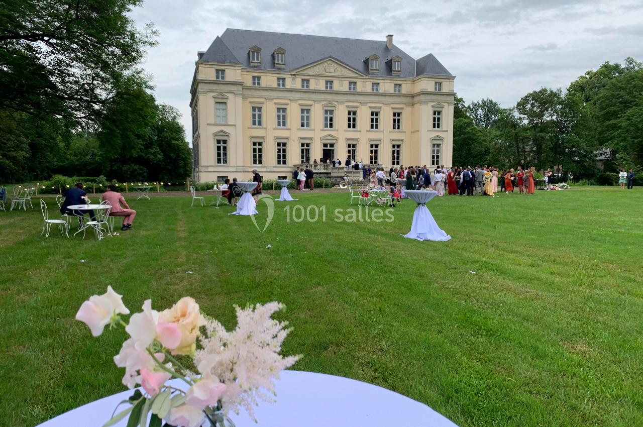Groupe de personnes rassemblées devant un château entouré d'un grand jardin, avec des tables décorées au premier plan.