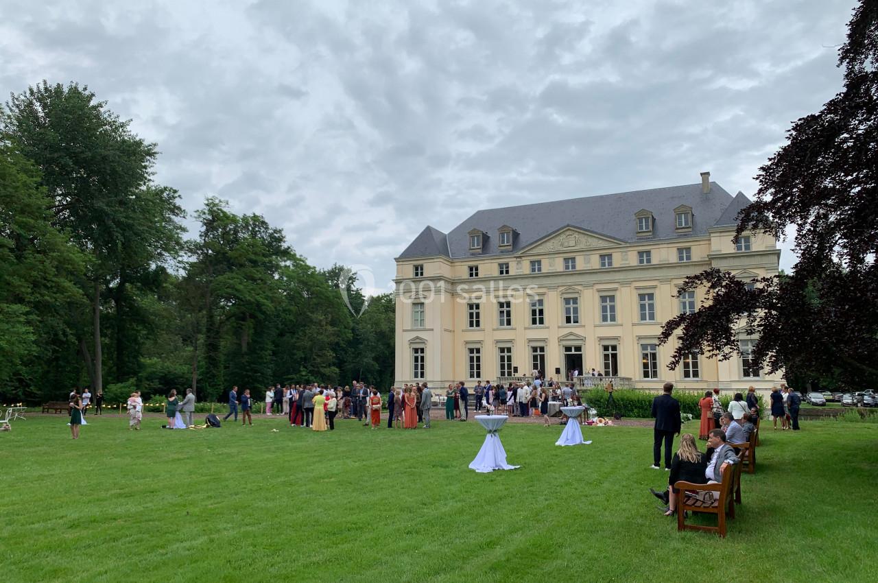 Groupe de personnes rassemblées sur une pelouse devant un grand bâtiment de style classique par temps nuageux.