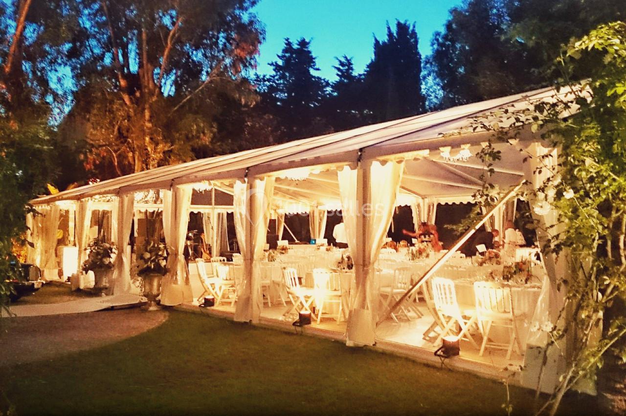 Tente blanche éclairée en soirée, aménagée avec des tables et chaises pour un événement en extérieur.