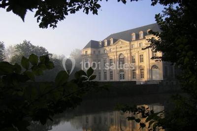 Salon lumineux avec parquet, mobilier classique, table ronde dressée au centre et lustre en cristal au plafond.